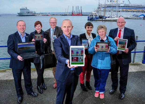 A group of individuals showcasing the new responsive website across multiple devices in the Falmouth harbour. The website was designed and built by Oracle Design