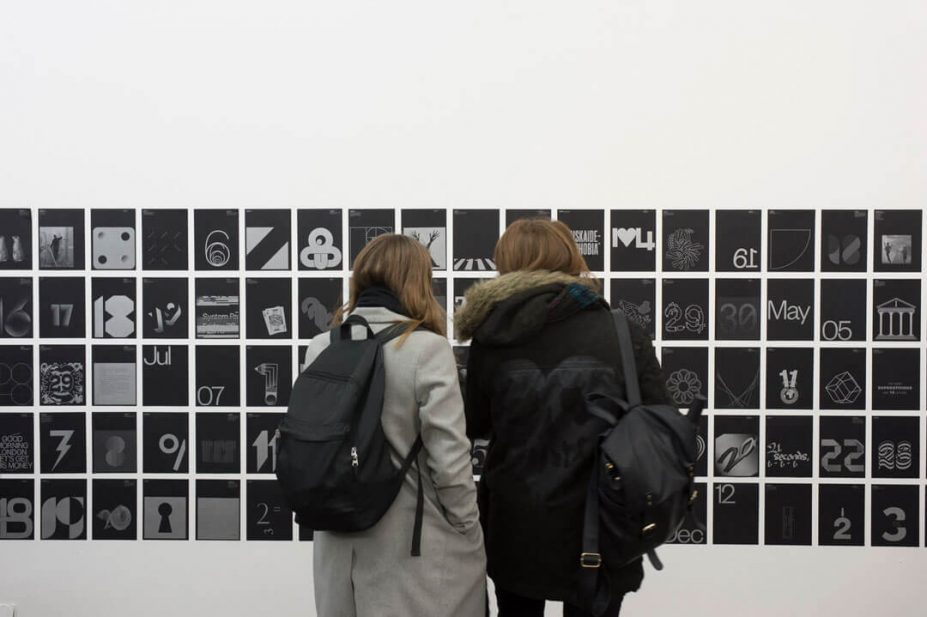Two people looking at a wall displaying the different pages from the Fedrigoni 365 calendar brochure.